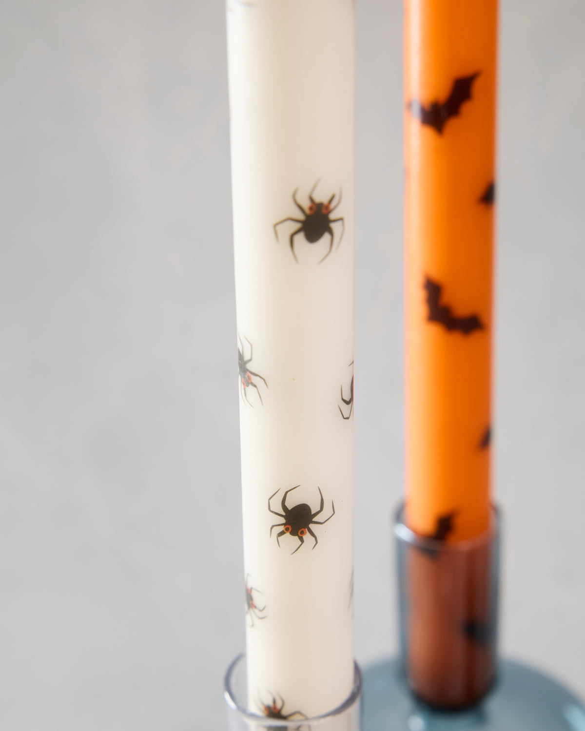 Close-up of an ivory spider-patterned taper candle beside an orange bat-patterned taper candle in candle holders.