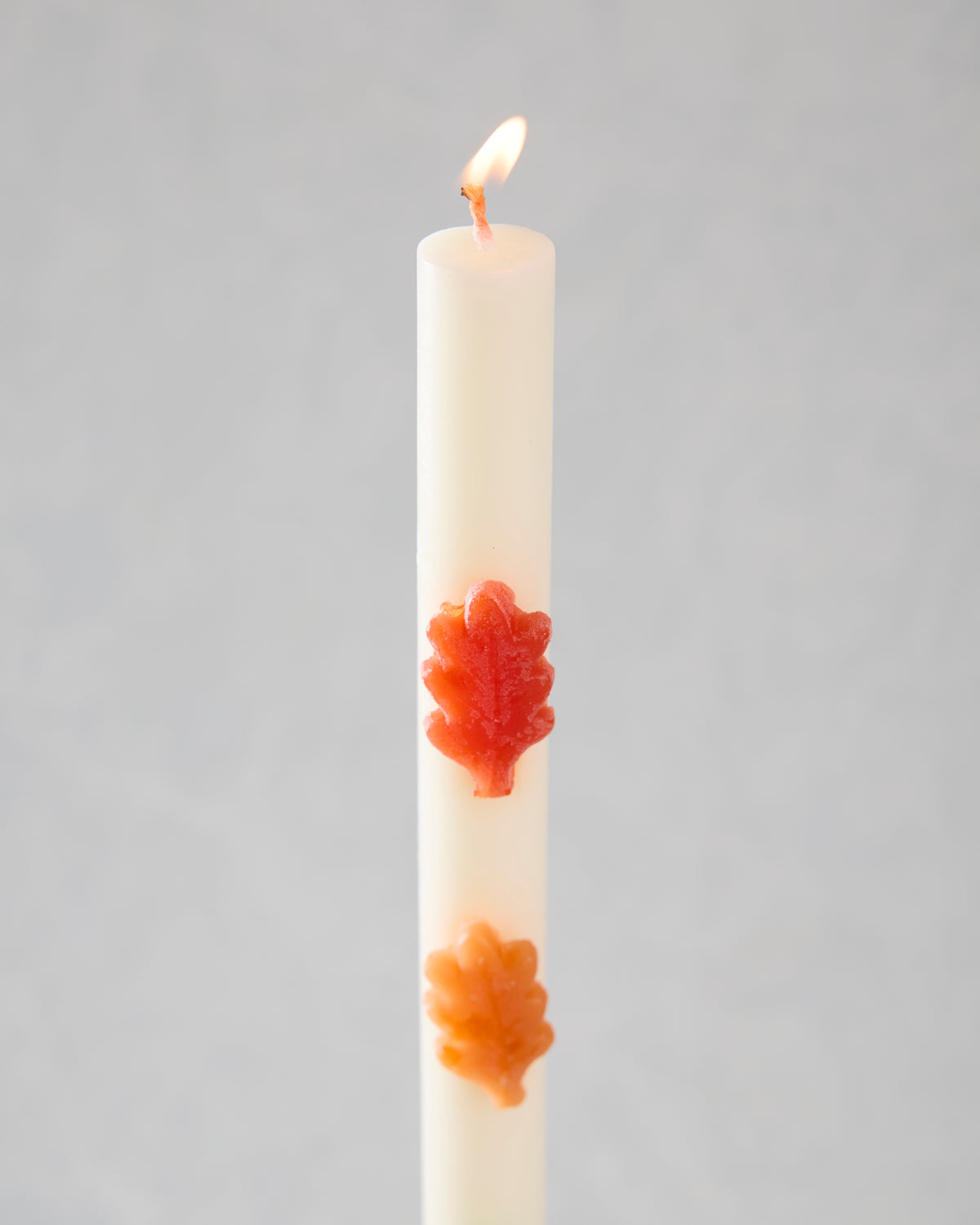 Lit white leaf-decorated candle with red-orange and orange leaf-shaped accents.