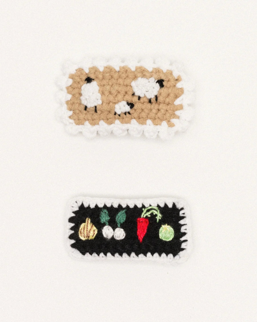 Two crochet snap hair clips displayed on a white background: one with sheep and one with vegetables.