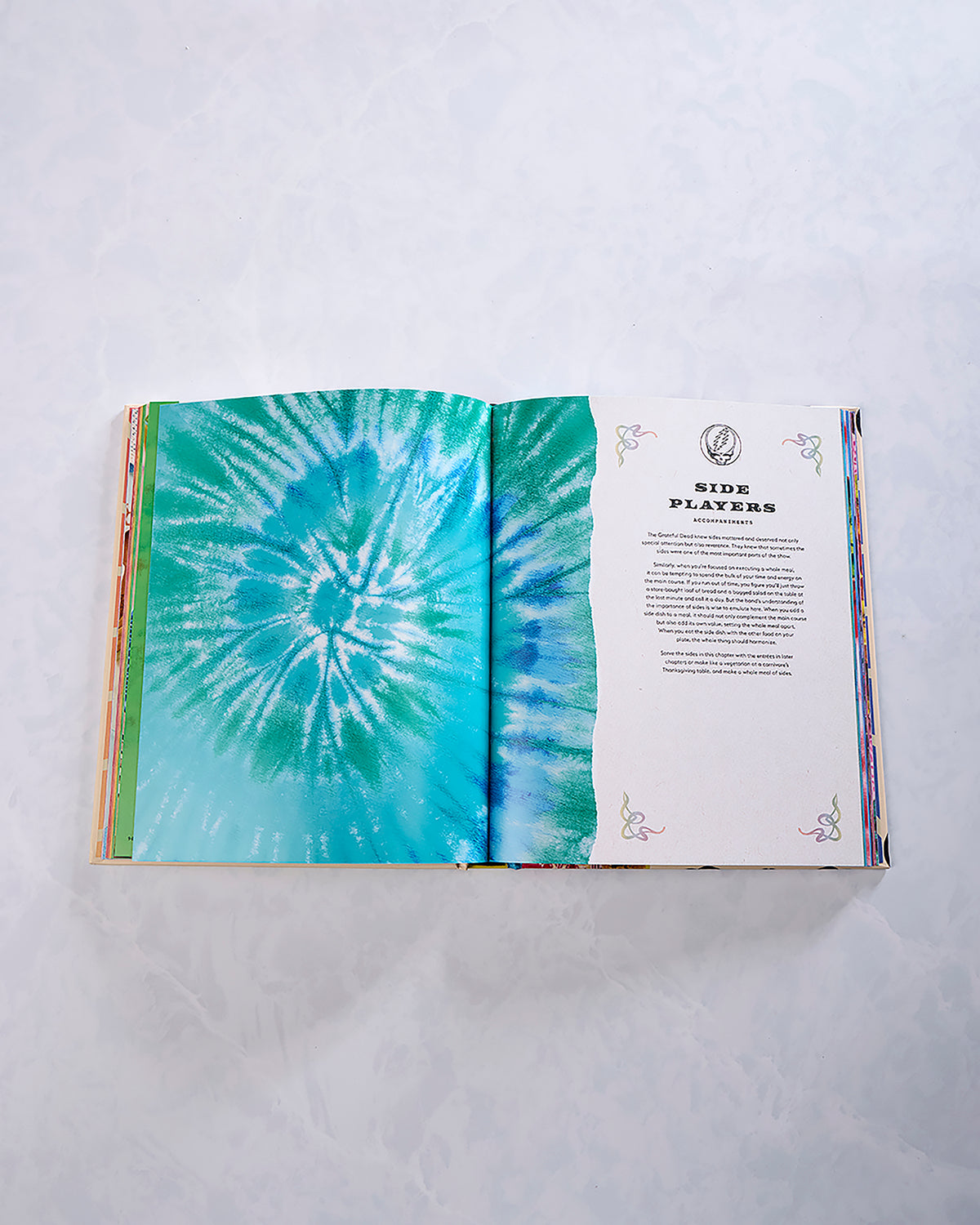 Open cookbook showing a turquoise tie-dye-style page beside a decorated text page headed “Side Players.”