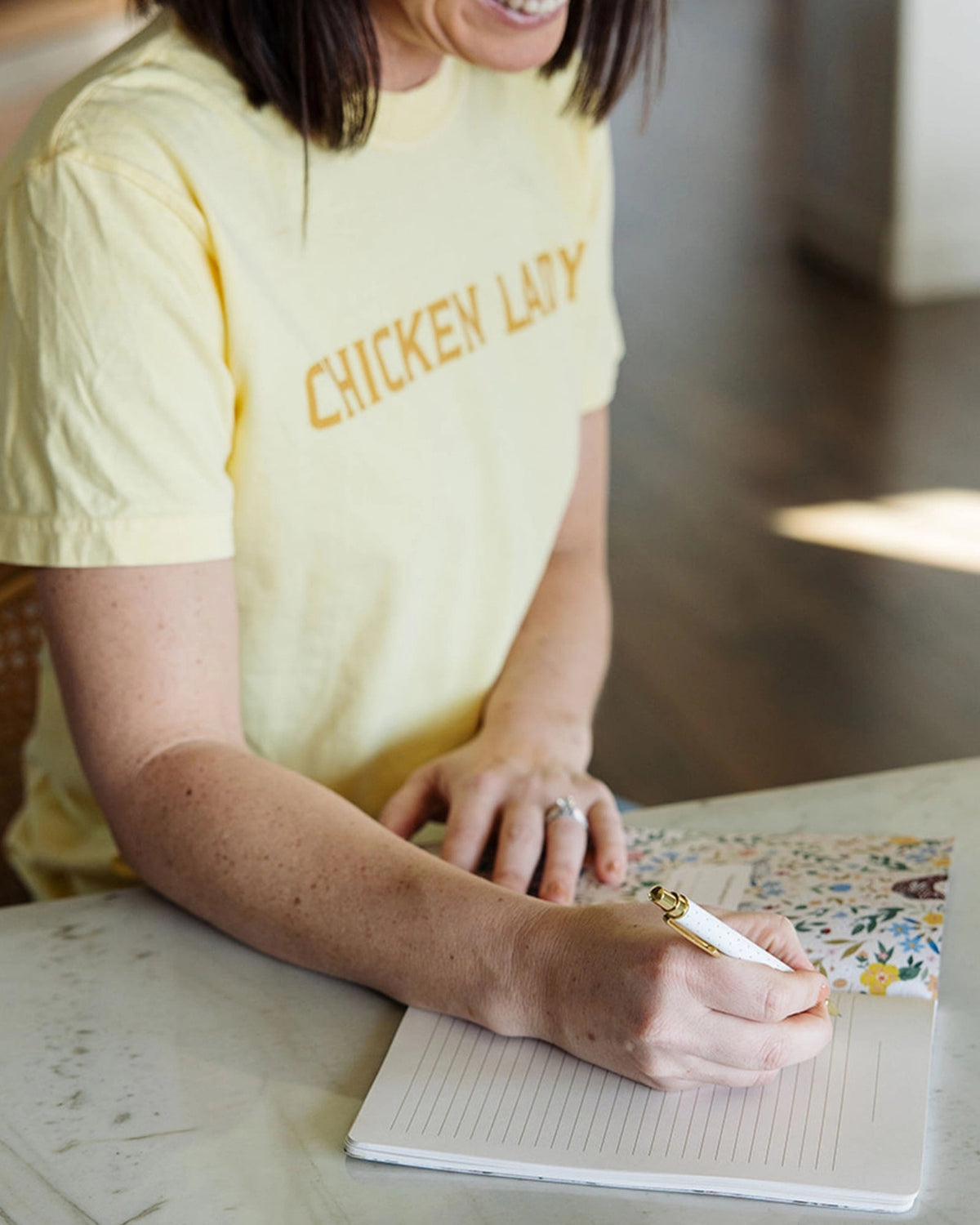 Person writing in a lined notebook decorated with chicken and flower illustrations.