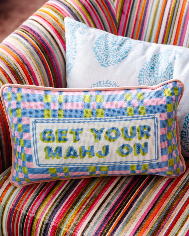 Needlepoint pillow reading “GET YOUR MAHJ ON” on a multicolored plaid chair.