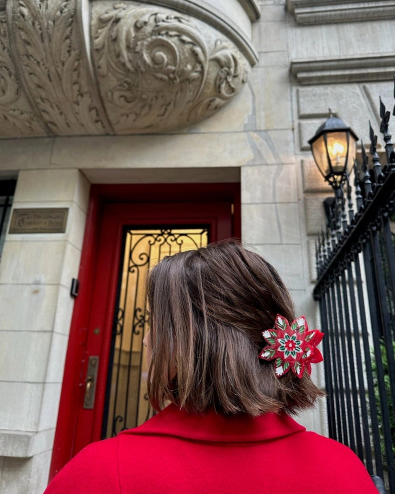 Christmas flower claw clip securing hair, shown from the rear near a red door.