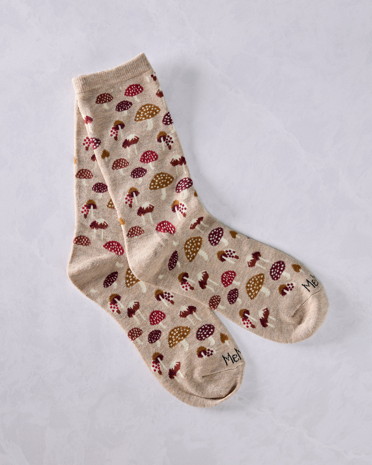 Two tan crew socks with a repeating mushroom pattern, overlapping on a light background.