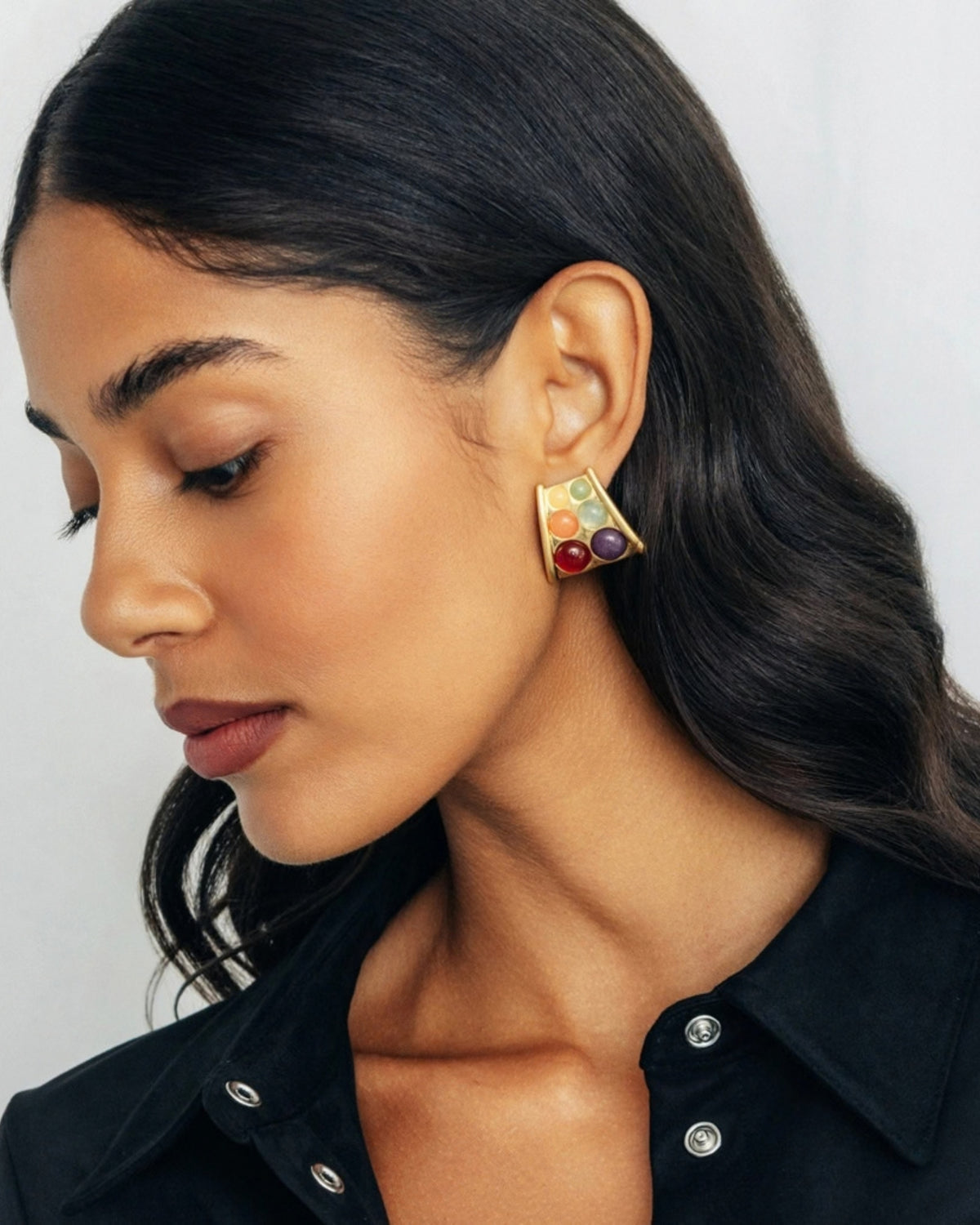 Close-up of a person wearing a triangular Beatrix earring with multicolored round stones