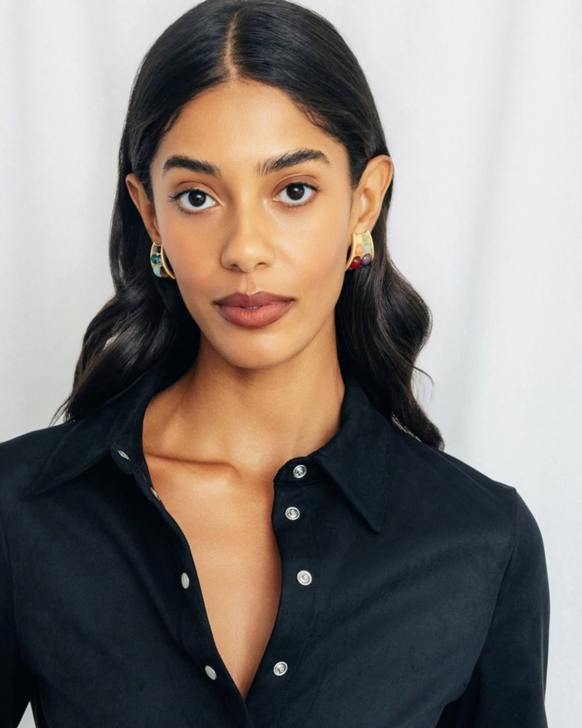 Front view of a person wearing matching triangular Beatrix earrings with multicolored round stones