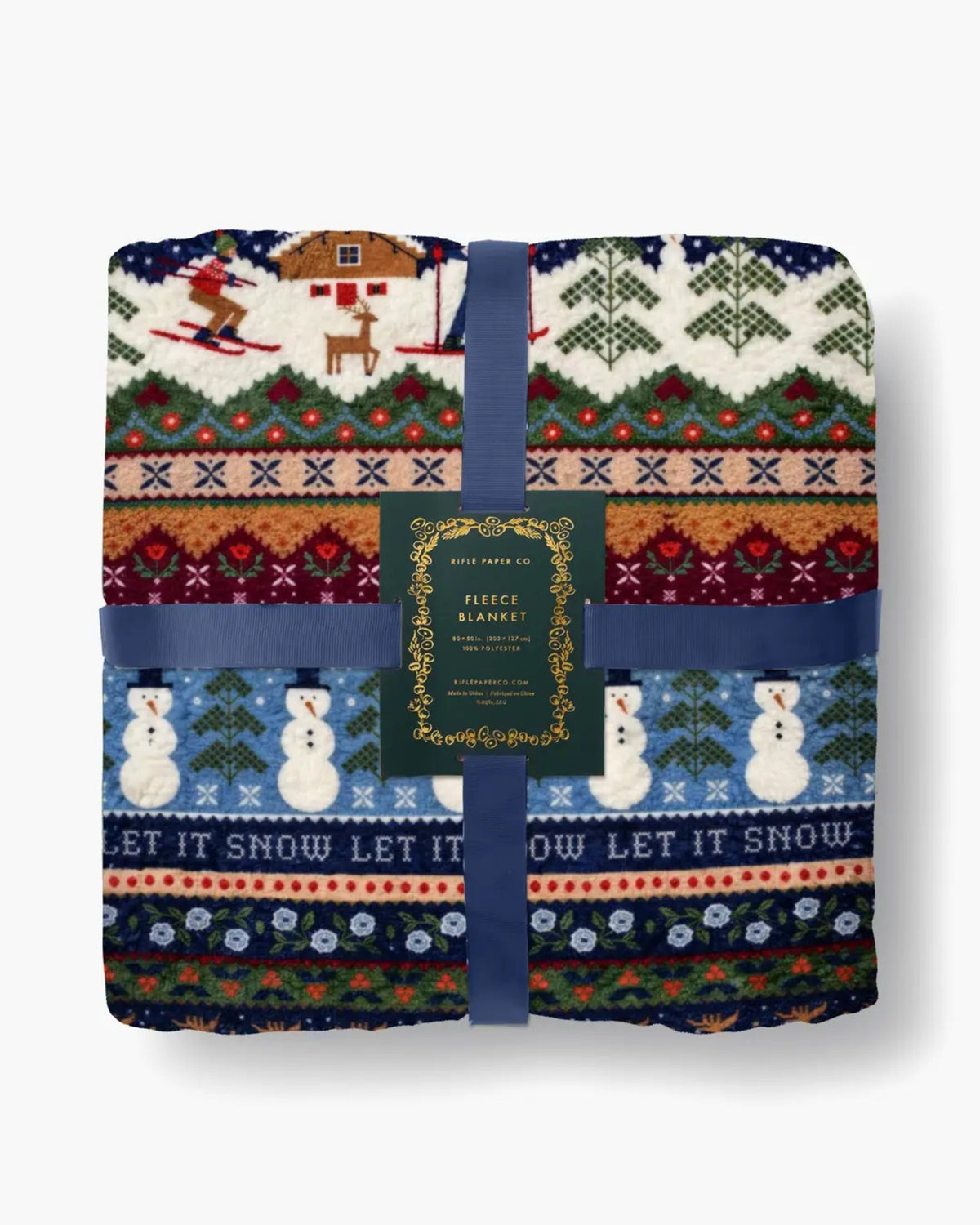 Folded Ski Chalet fleece blanket in a winter sweater-style pattern, packaged with blue ribbon and a label reading “RIFLE PAPER CO. FLEECE BLANKET.”