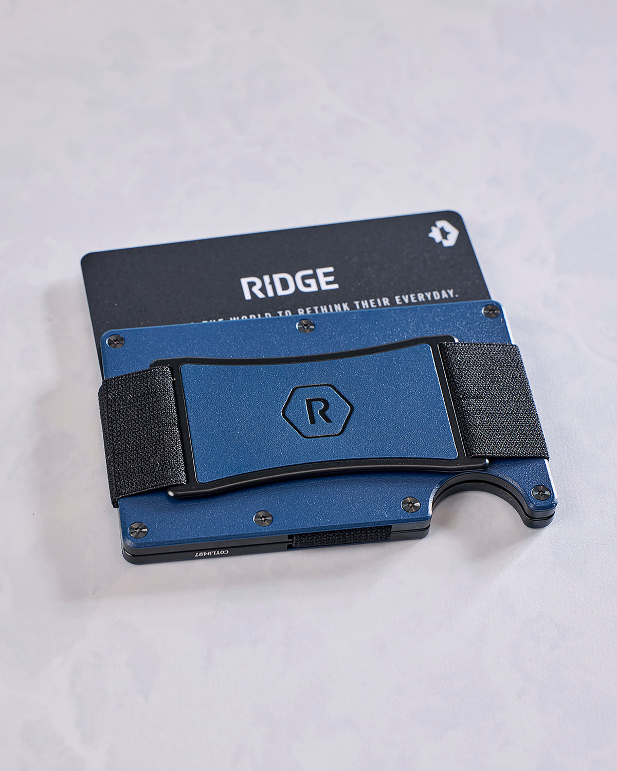 Front view of a navy Ridge wallet with a black elastic cash strap, logo panel, and card partially visible behind it.