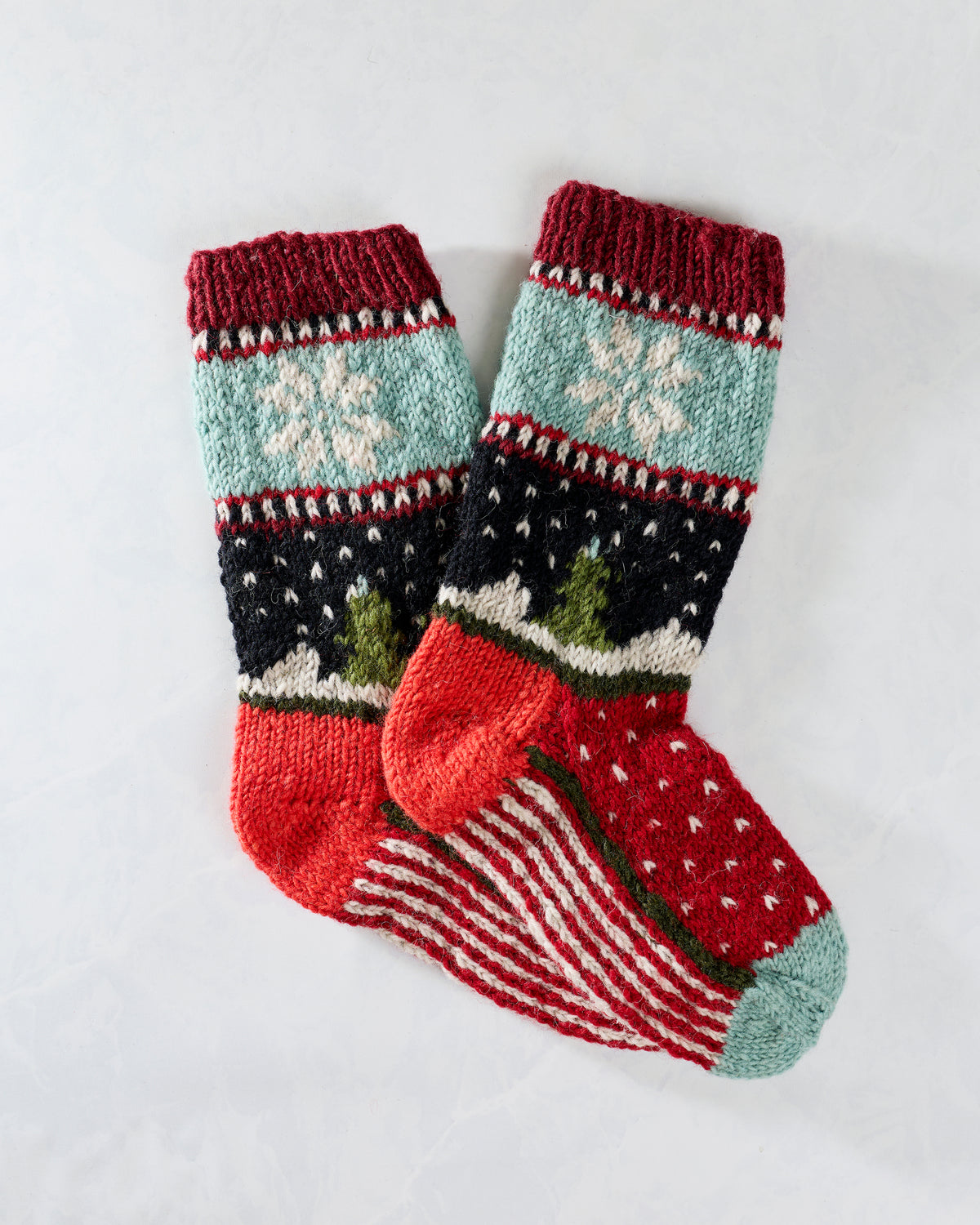 Pair of multicolored knitted holiday socks with snowflakes, trees, and patterned stripes.