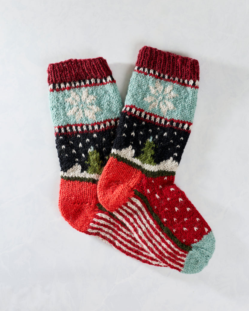 Pair of multicolored knitted holiday socks with snowflakes, trees, and patterned stripes.