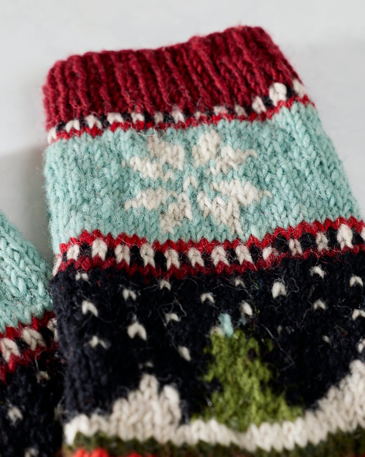 Close-up of a knitted holiday sock showing a white snowflake on a light blue cuff above patterned bands.