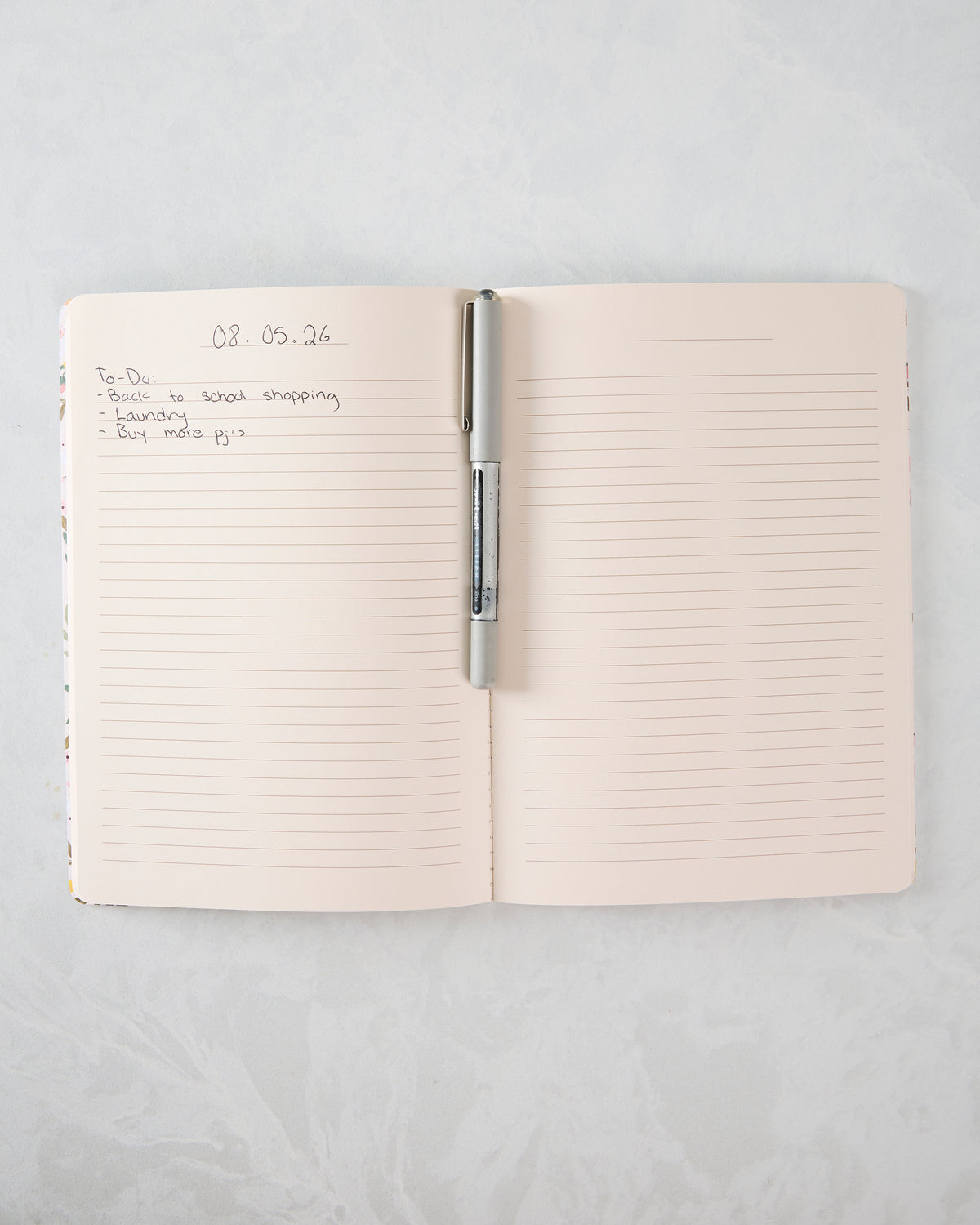 Open lined notebook with a pen across the center fold and a handwritten to-do list on the left page.