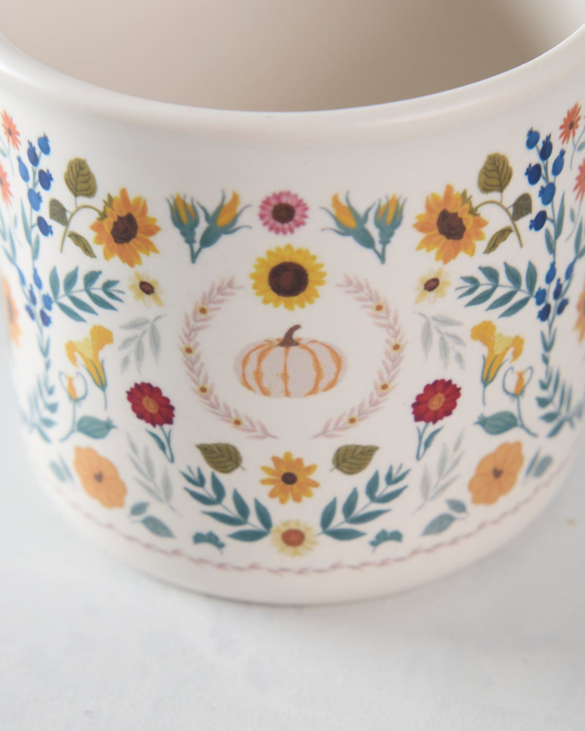 Close-up of the ceramic mug's pumpkin, sunflower, floral, leaf, and blue berry design.