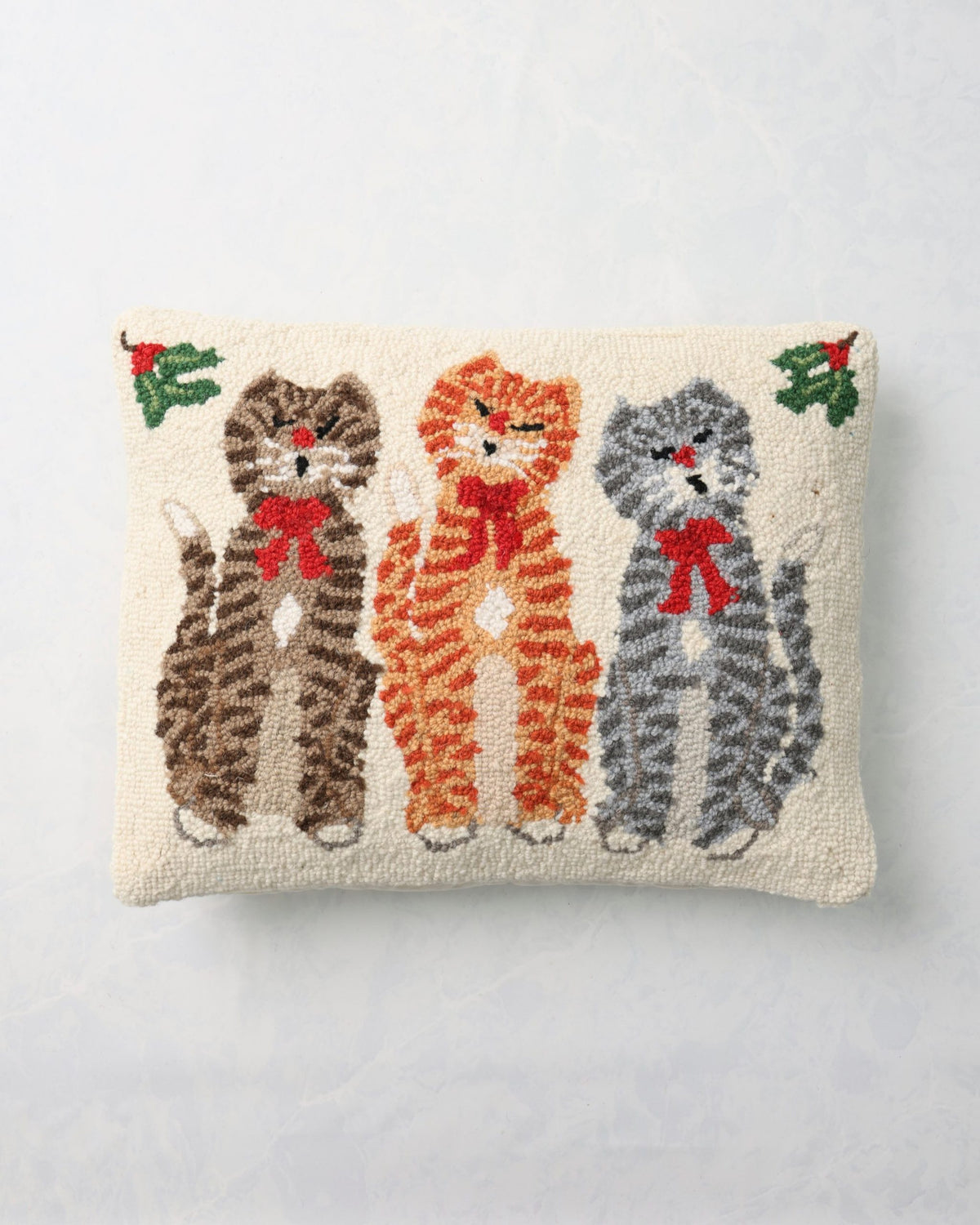 Front of a hooked pillow depicting three cats wearing red bows.