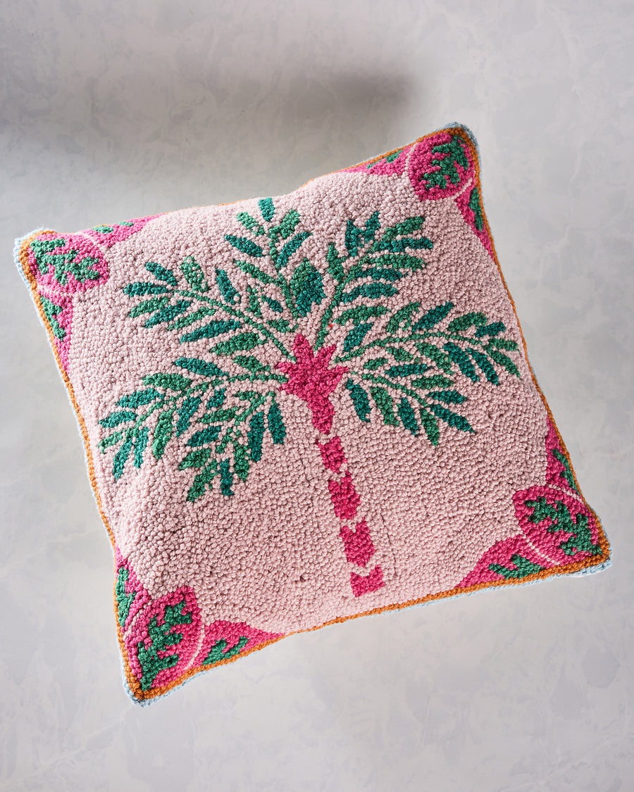 Pink square hook pillow with a central green palm tree and colorful patterned corner motifs.