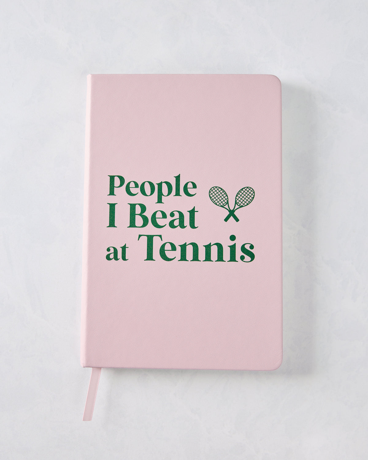 Front cover of a pink journal reading “People I Beat at Tennis,” with a crossed-rackets icon.