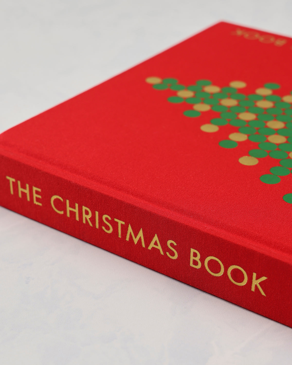 Close angled view of the red clothbound Christmas Book cover and spine, showing the gold title lettering and part of the tree design.