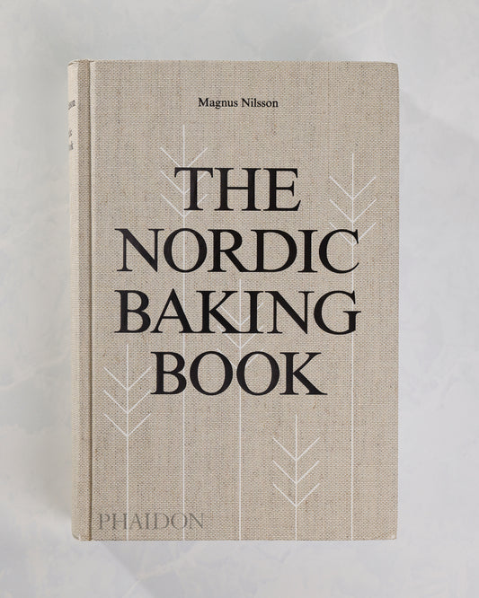 Front cover of The Nordic Baking Book by Magnus Nilsson, featuring large black title lettering and white stylized tree outlines on a light background.
