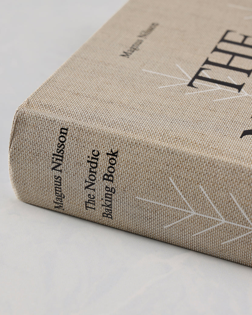 Close angled view of The Nordic Baking Book showing its clothbound cover, spine, black title lettering, and white tree-line design.