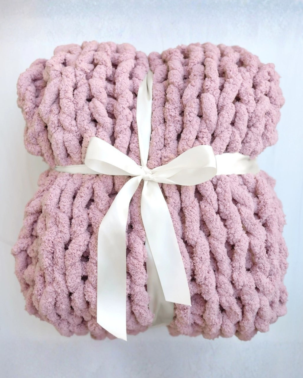 Pink chunky knit blanket folded and tied with a white ribbon.