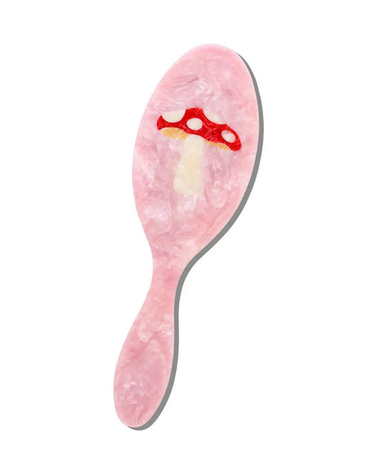Front view of a pink handled brush with a red mushroom design.