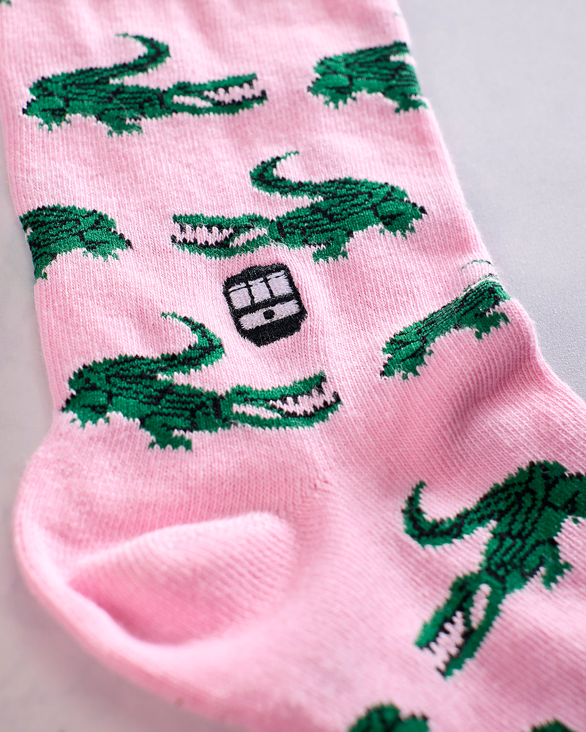 Close-up of pink socks with repeating green alligator designs and a black Bonfolk logo.