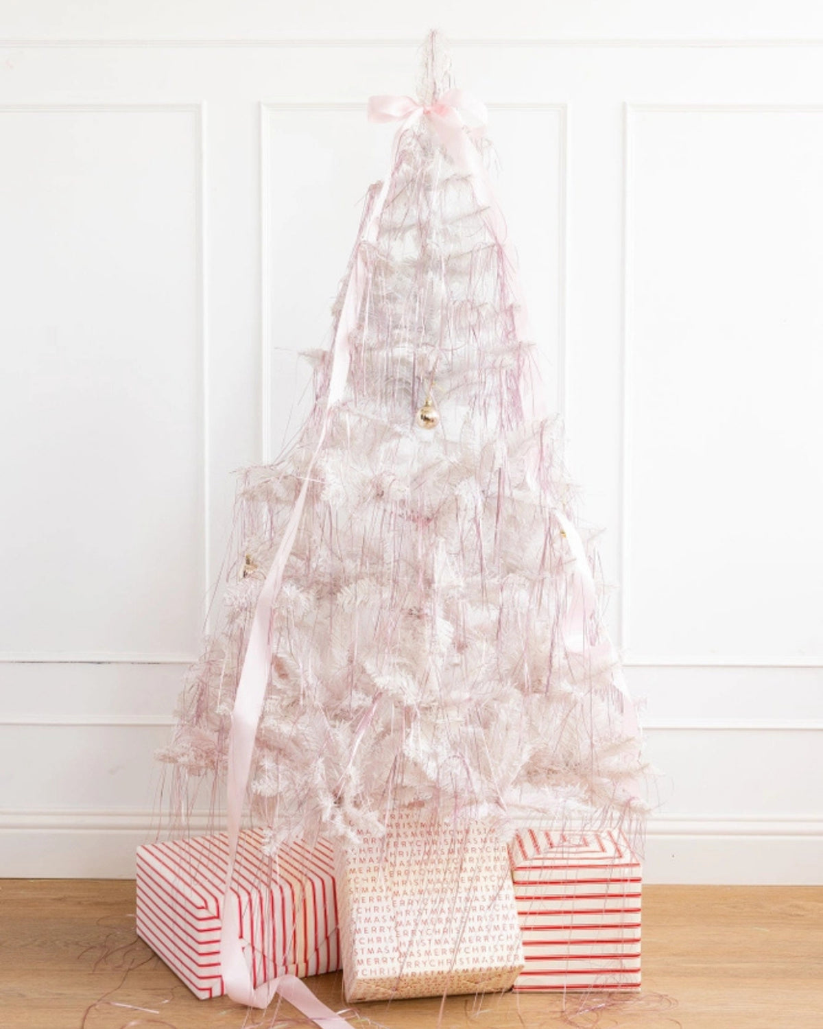 Pink tinsel arranged as a sparse Christmas tree with pink ribbon, ornaments, and wrapped gifts at the base.