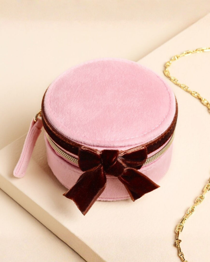 Closed pink round travel jewelry case with a brown bow and gold zipper.