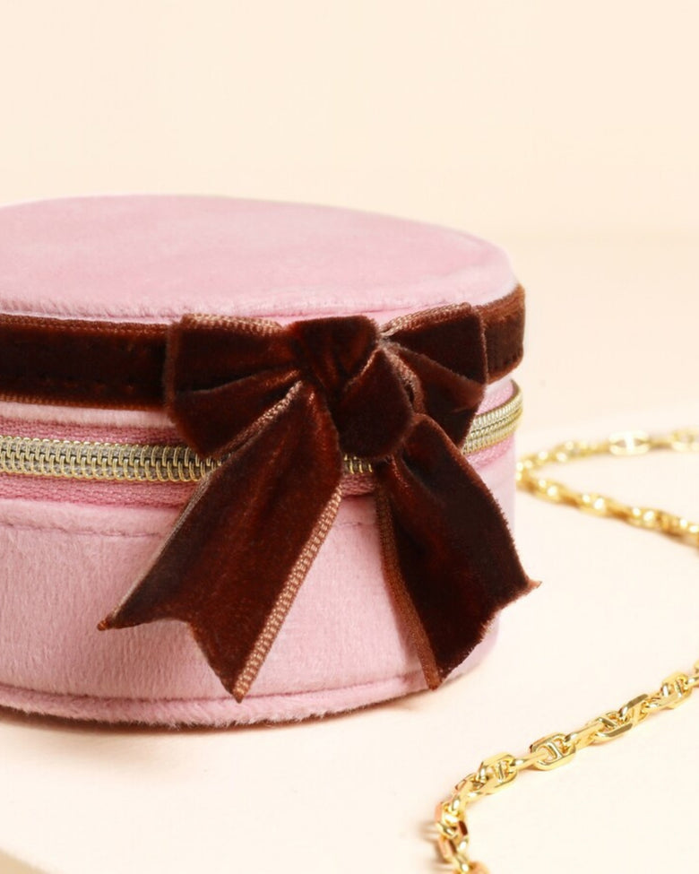 Close-up of the closed pink round travel jewelry case with a brown velvet bow and gold zipper.