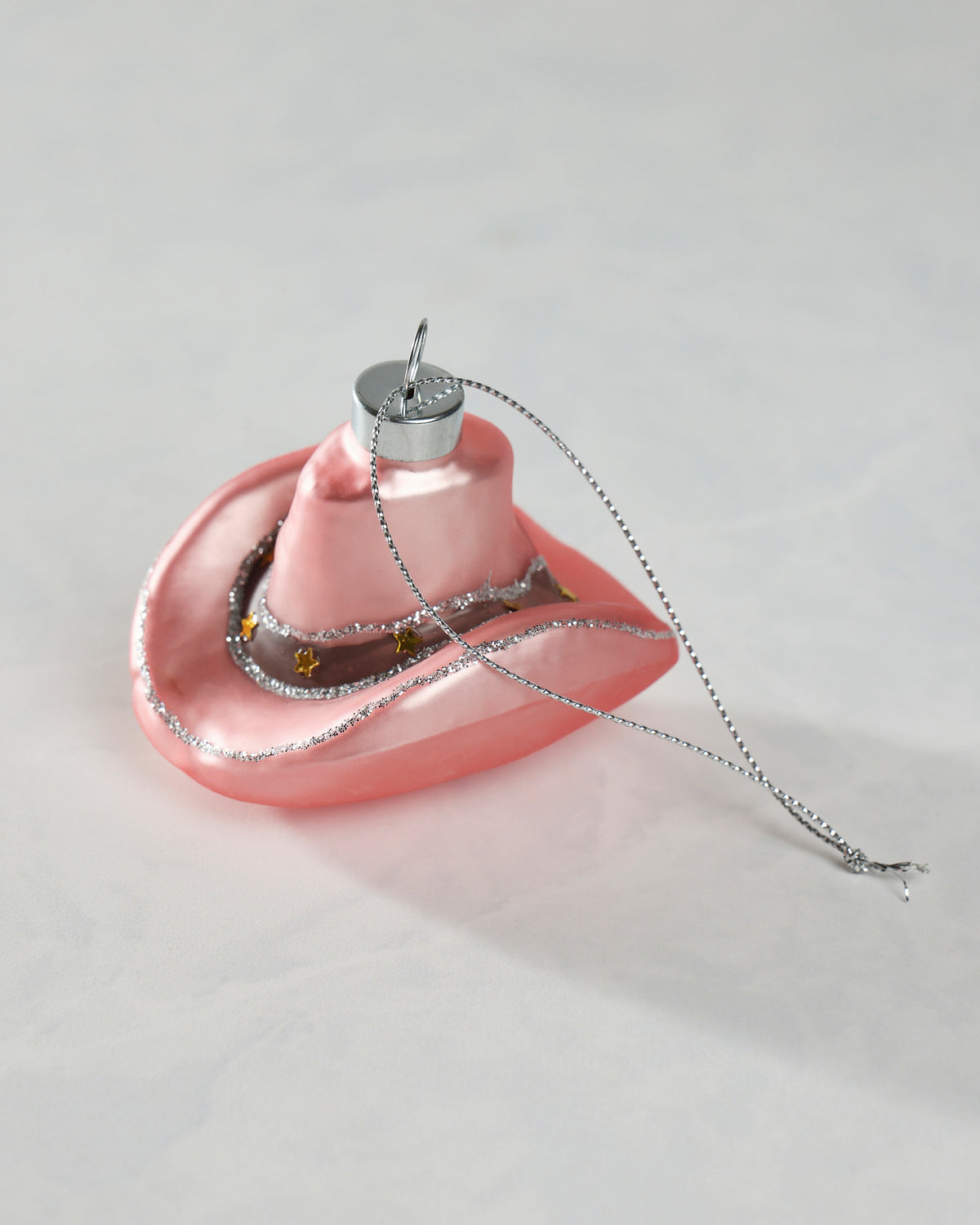 Pink cowgirl hat glass ornament with silver glitter trim, gold star accents, and a hanging loop.