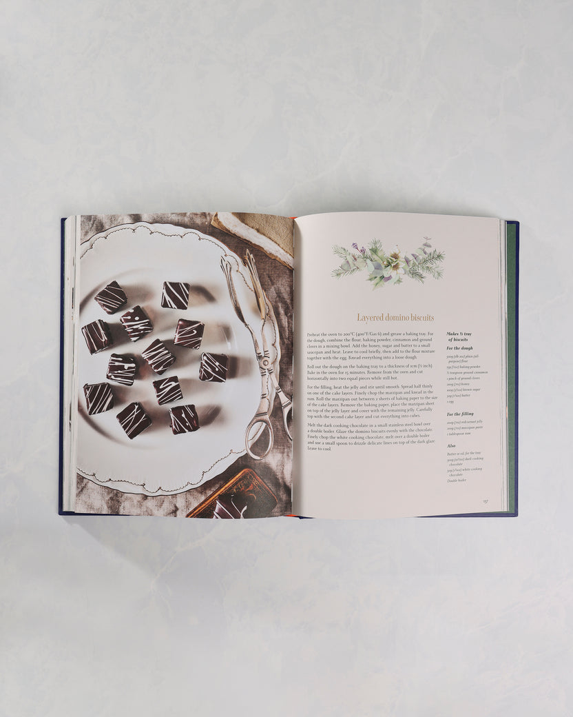 Open Christmas cookbook showing a page titled Layered domino biscuits beside a photograph of chocolate-dipped square biscuits on a serving plate.