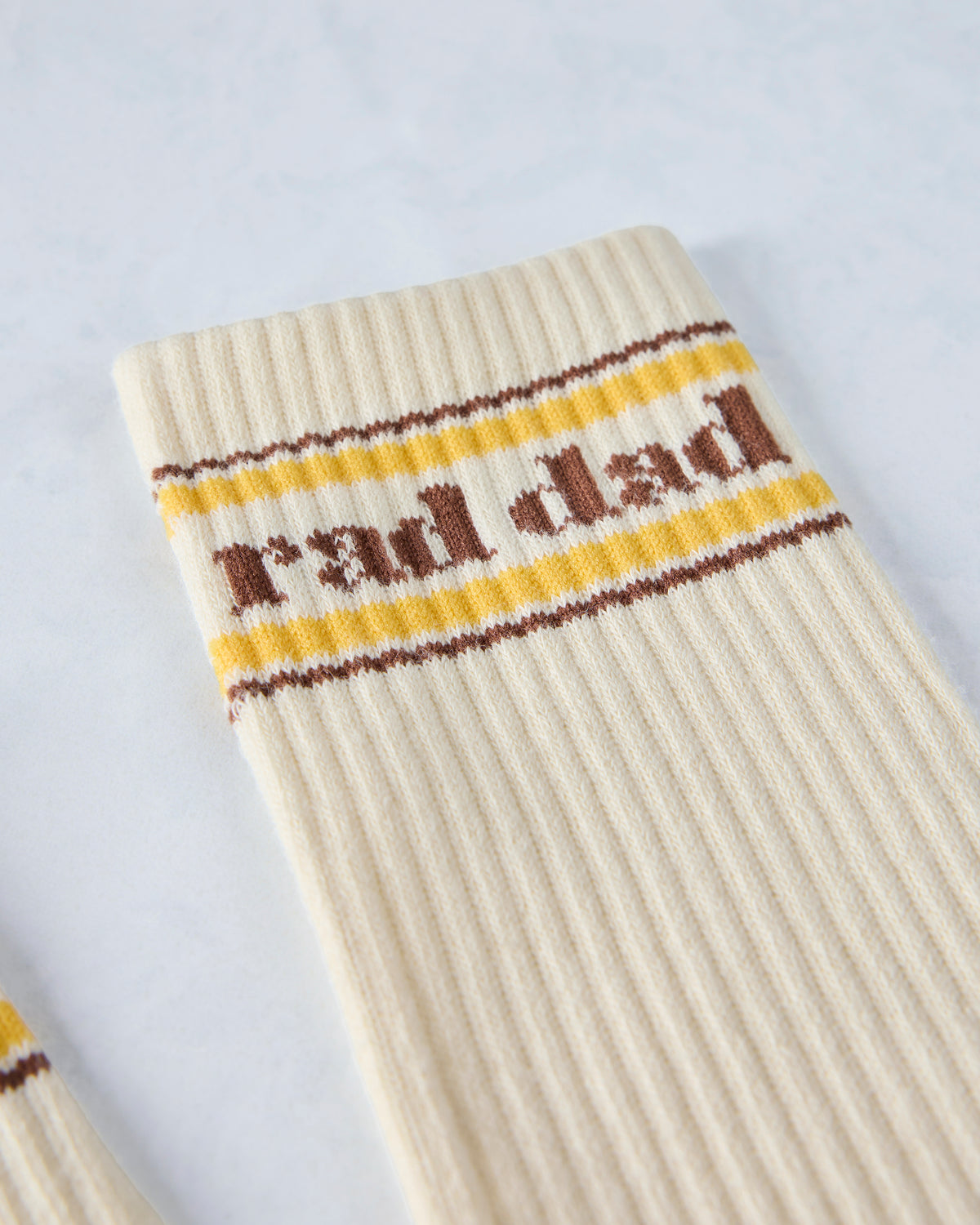 Close-up of an ivory sock cuff with brown and yellow stripes and “Rad Dad” lettering.
