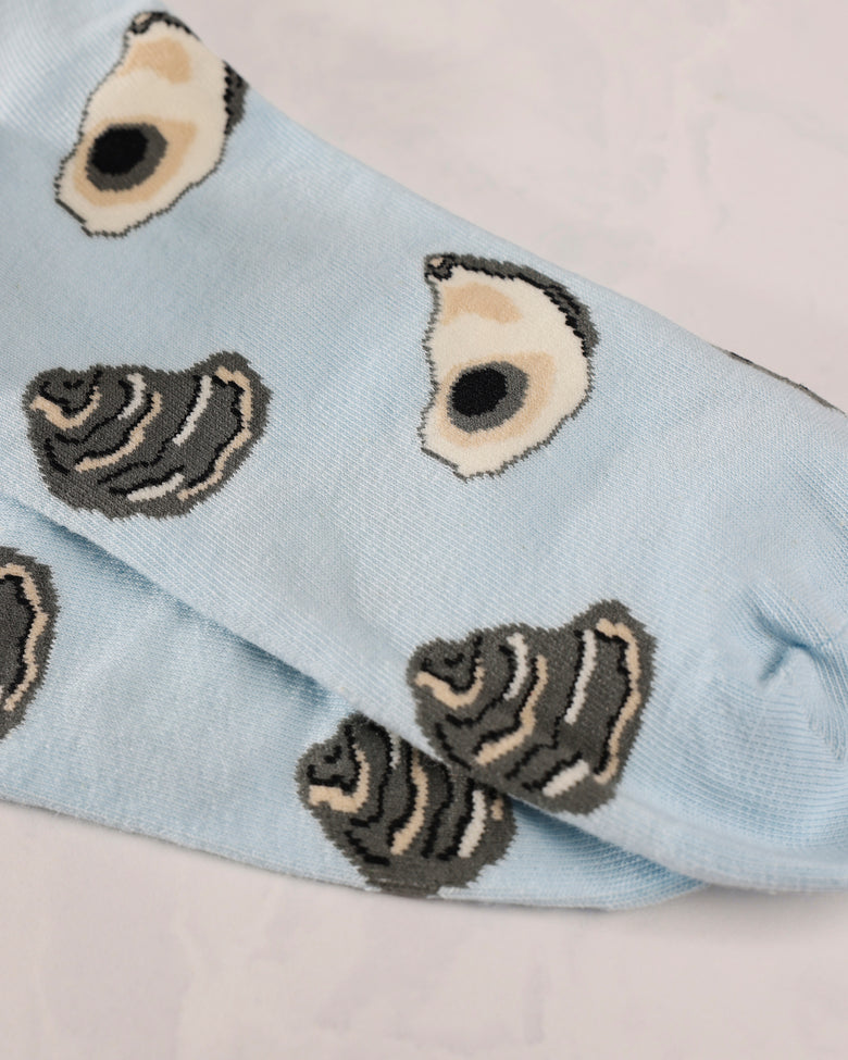 Close-up of light blue socks with repeating oyster shell and dark shell motifs.