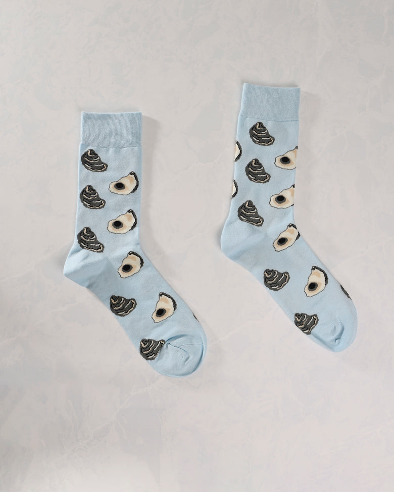 Pair of light blue socks with repeating oyster shell and dark shell motifs.