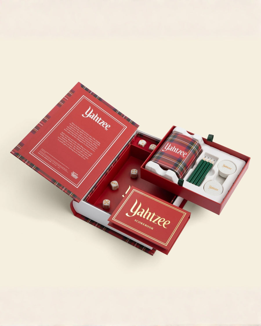 Open Yahtzee bookshelf game case showing the red rolling tray, dice, plaid dice cup, pencils, chips, and scorebook.