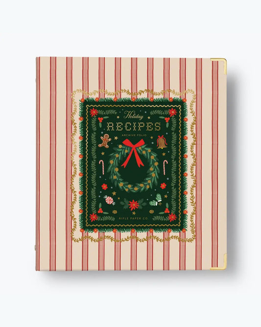 Closed red-striped holiday recipe binder with an illustrated wreath cover and gold-tone corner protectors.
