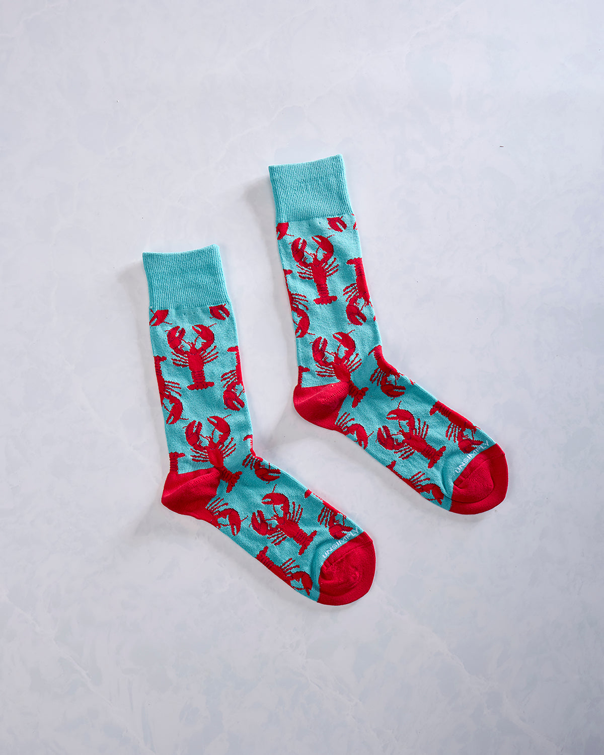 Pair of turquoise socks with repeating red lobster designs and red toes and heels.