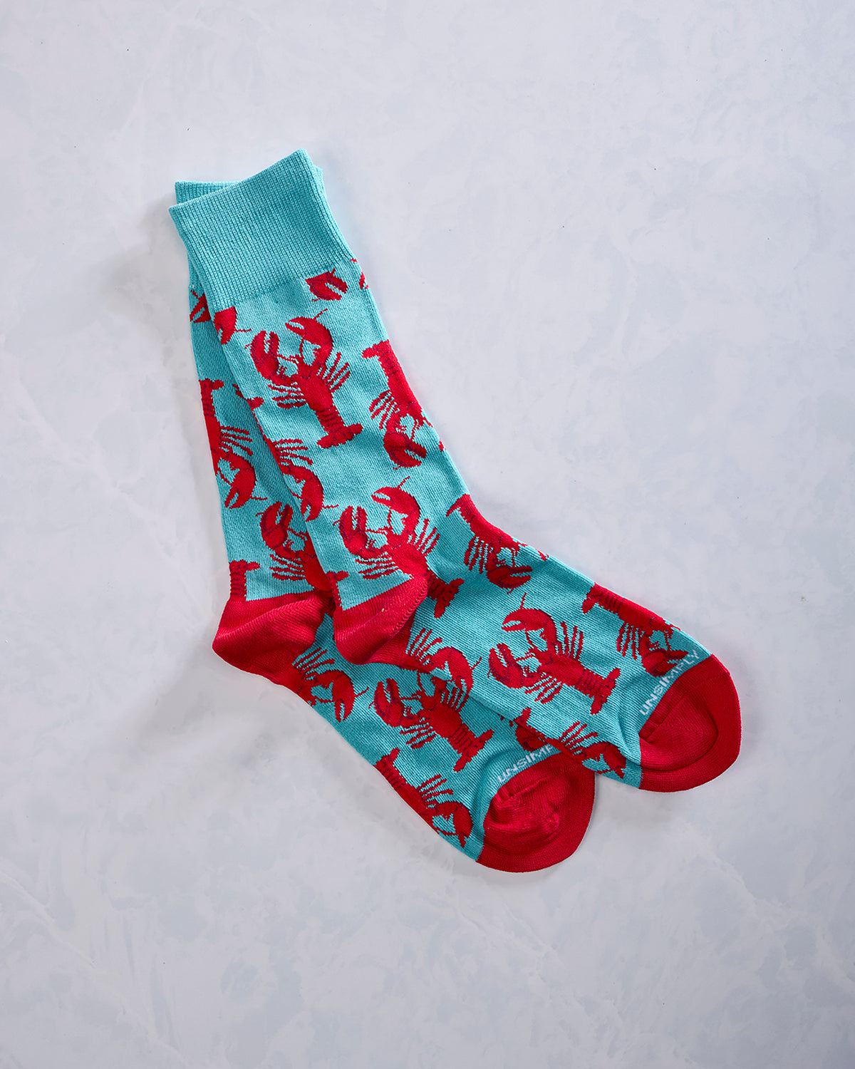 Pair of turquoise socks covered with repeating red lobster designs and red toe and heel accents.