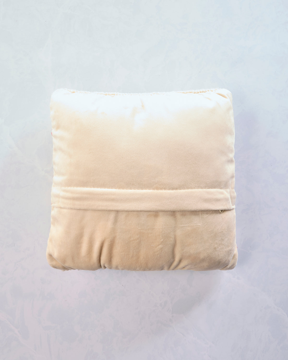 Back of the square red-and-cream striped pillow with a cream-colored backing and horizontal seam.