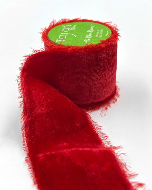 Roll of red wine silk velvet frayed ribbon with a loose length extending across a white background.