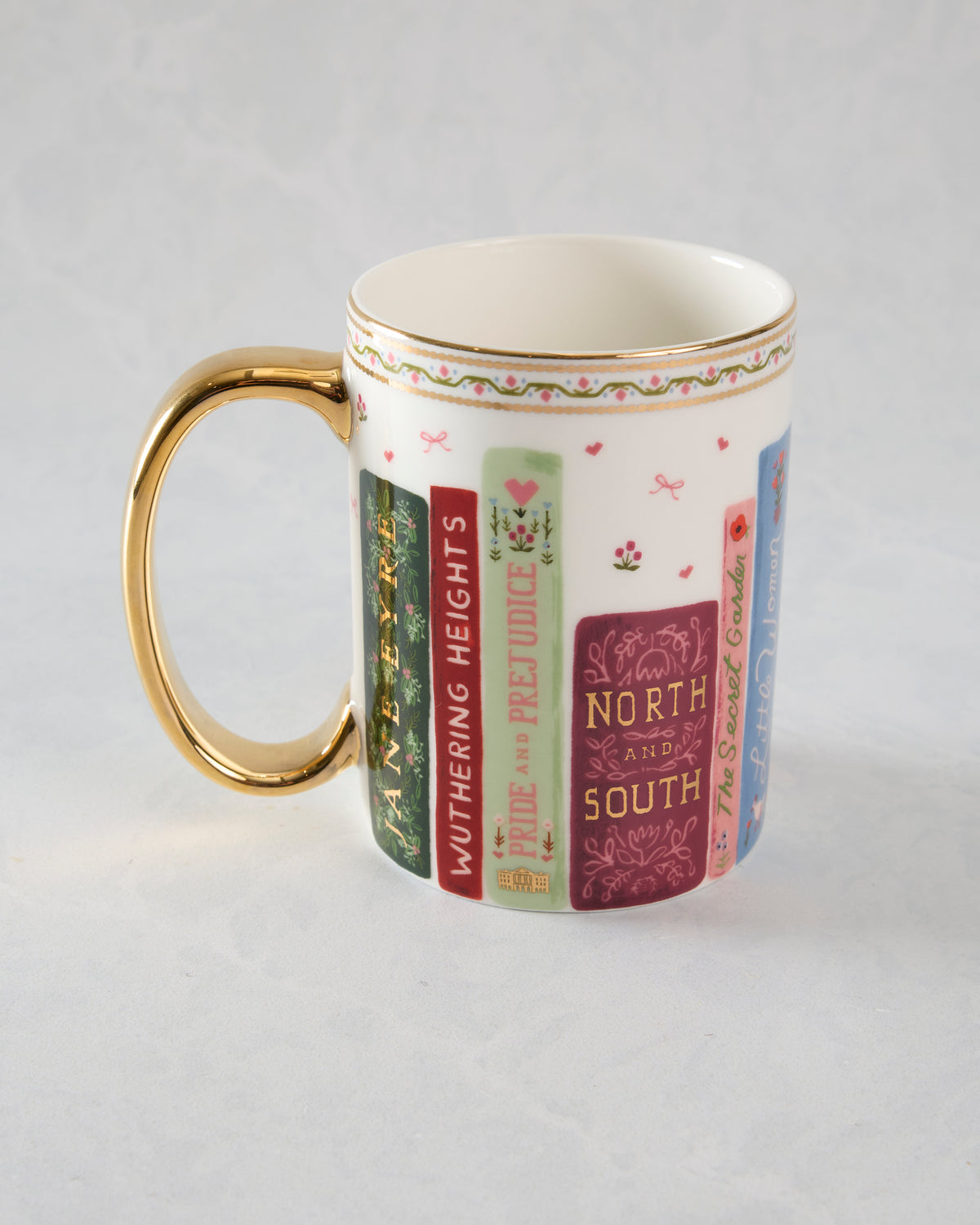 White porcelain mug with a gold handle, showing illustrated book spines including Wuthering Heights, Pride and Prejudice, and North and South.