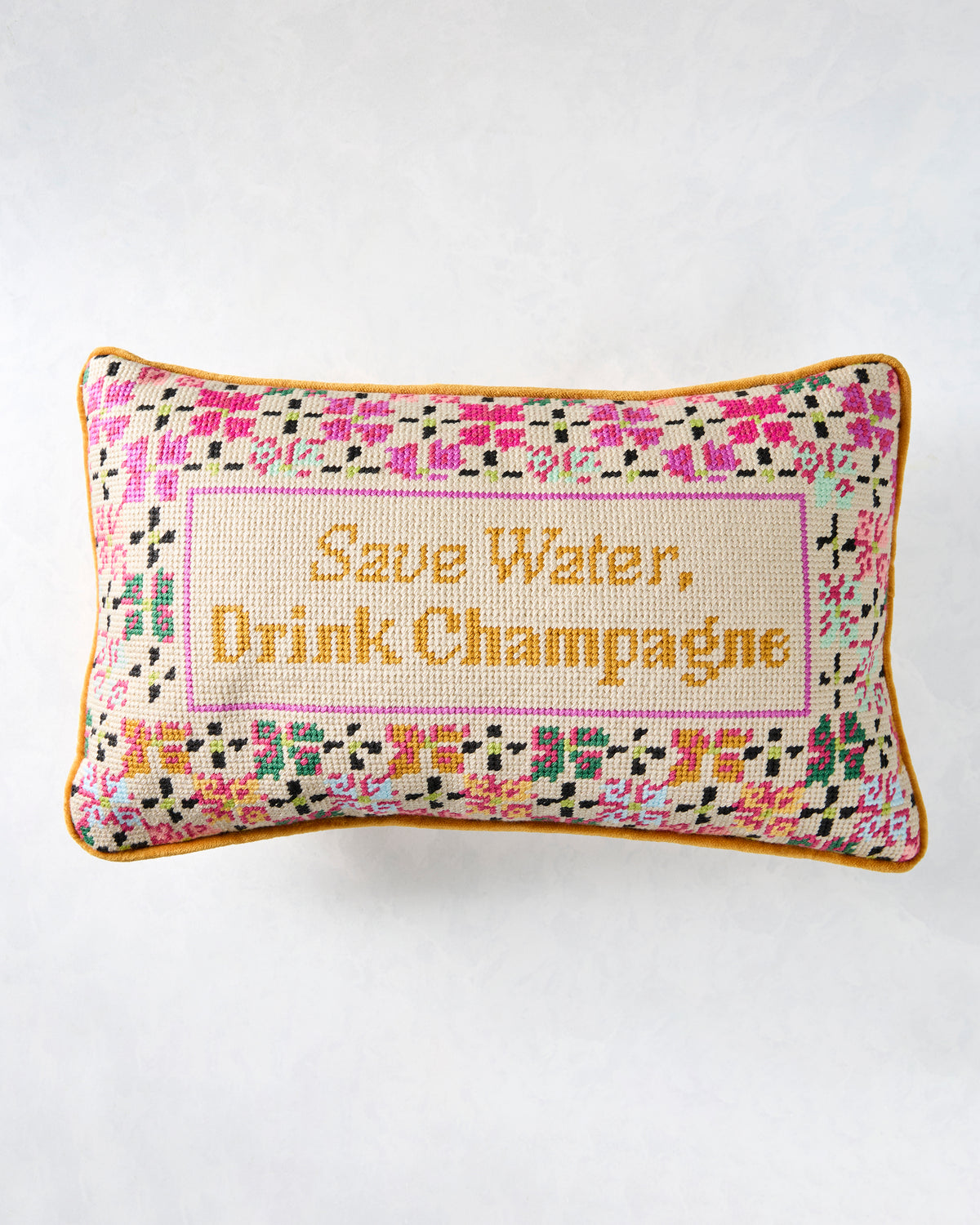 Rectangular needlepoint pillow with a multicolored floral border and the text “Save Water, Drink Champagne.”