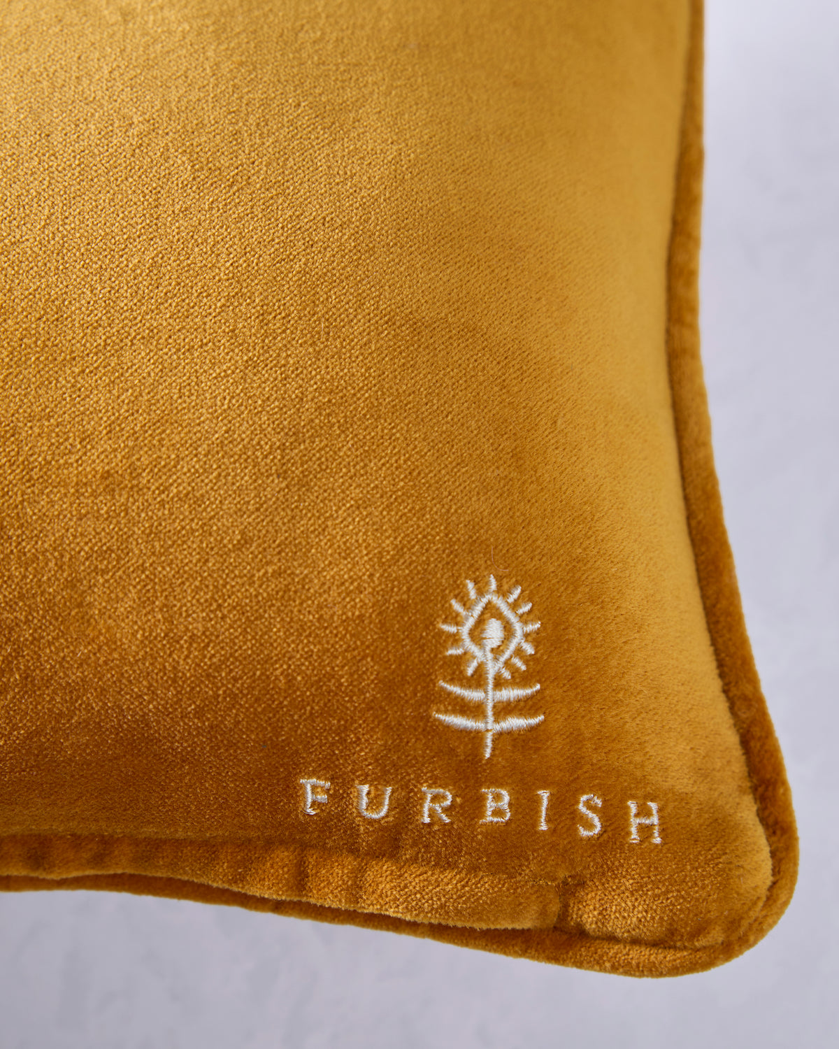 Close-up of the mustard velvet back of a needlepoint pillow with the Furbish logo.