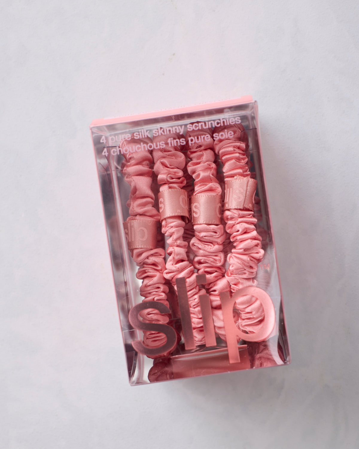 Close-up of four rose skinny scrunchies arranged inside Slip packaging.