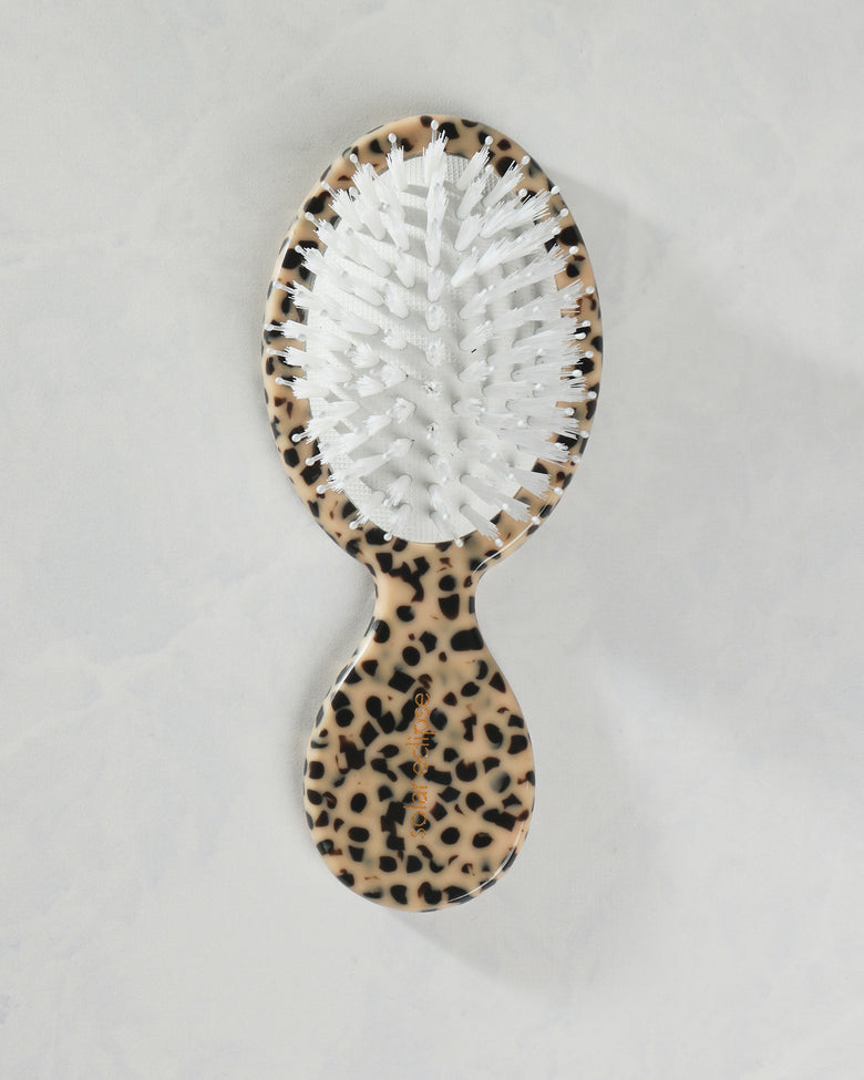 Front view of a leopard-pattern handbag hairbrush with white dual bristles and a compact rounded handle.
