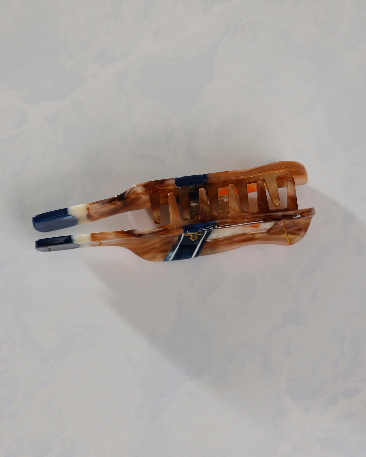 Side view of a bottle-shaped citrus spritz claw hair clip, showing its interlocking claw teeth, navy and amber design, and citrus emblem.