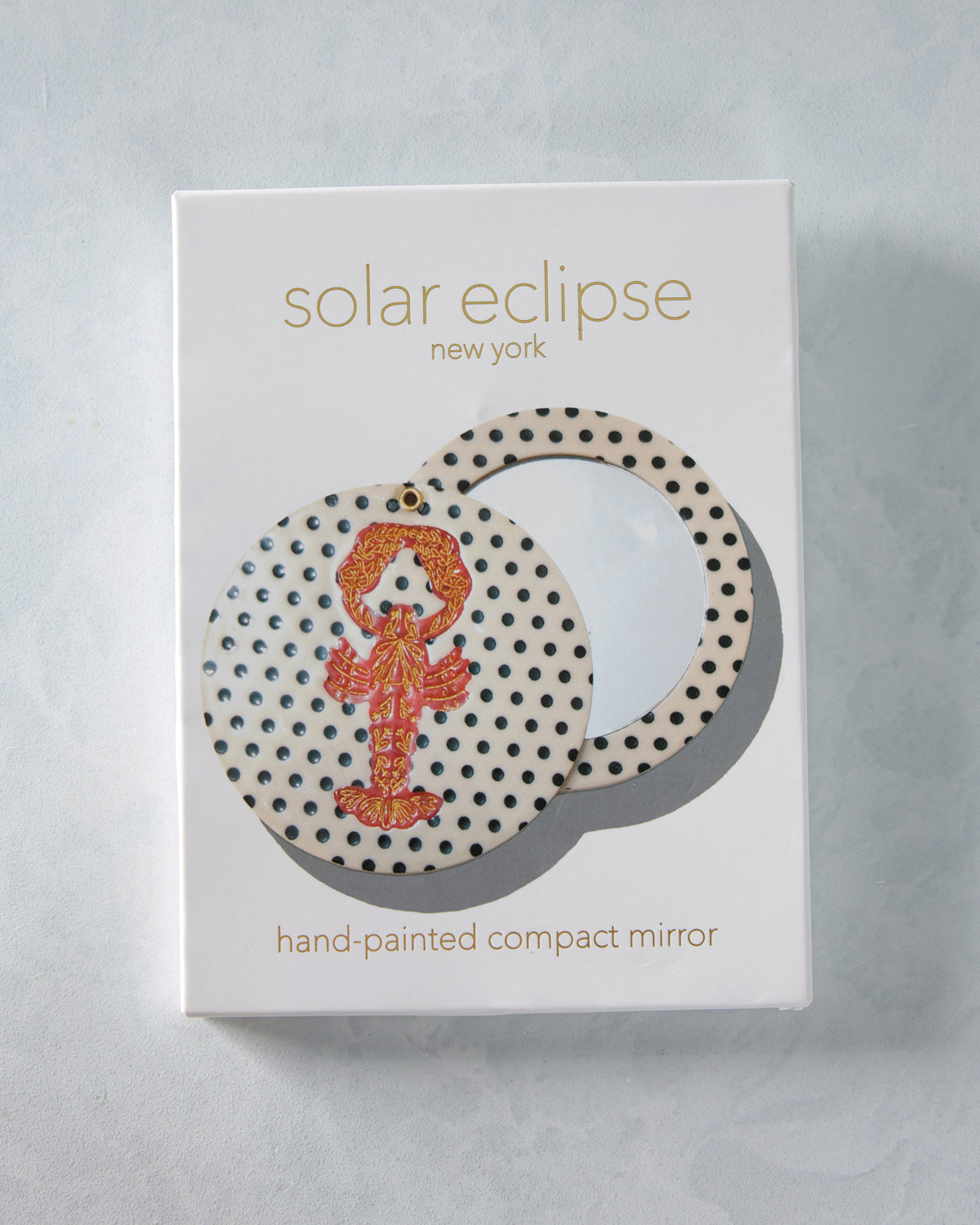 Packaged hand-painted lobster compact mirror with a cream cover covered in black dots.