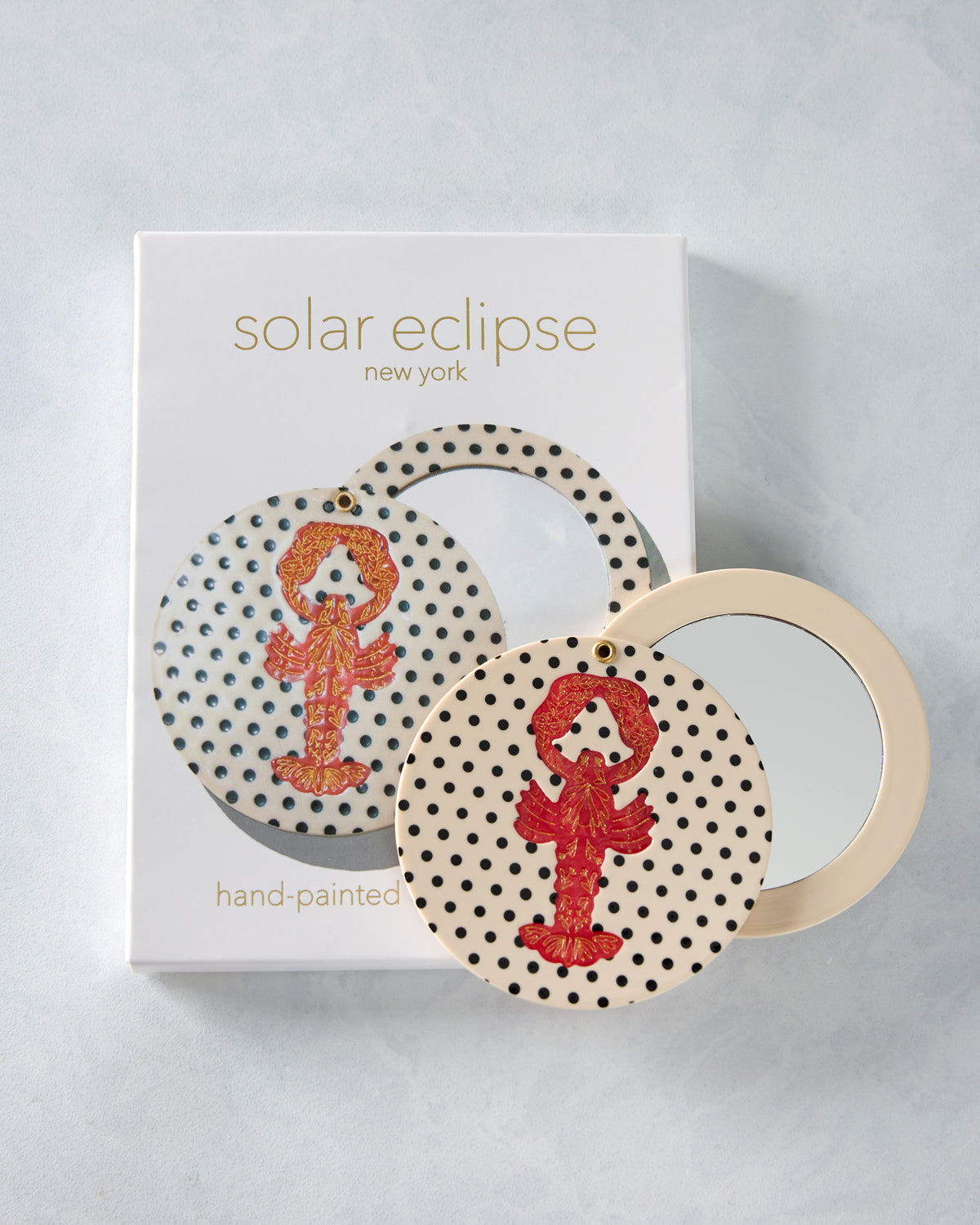 Hand-painted lobster compact mirror displayed open in front of its Solar Eclipse New York packaging.