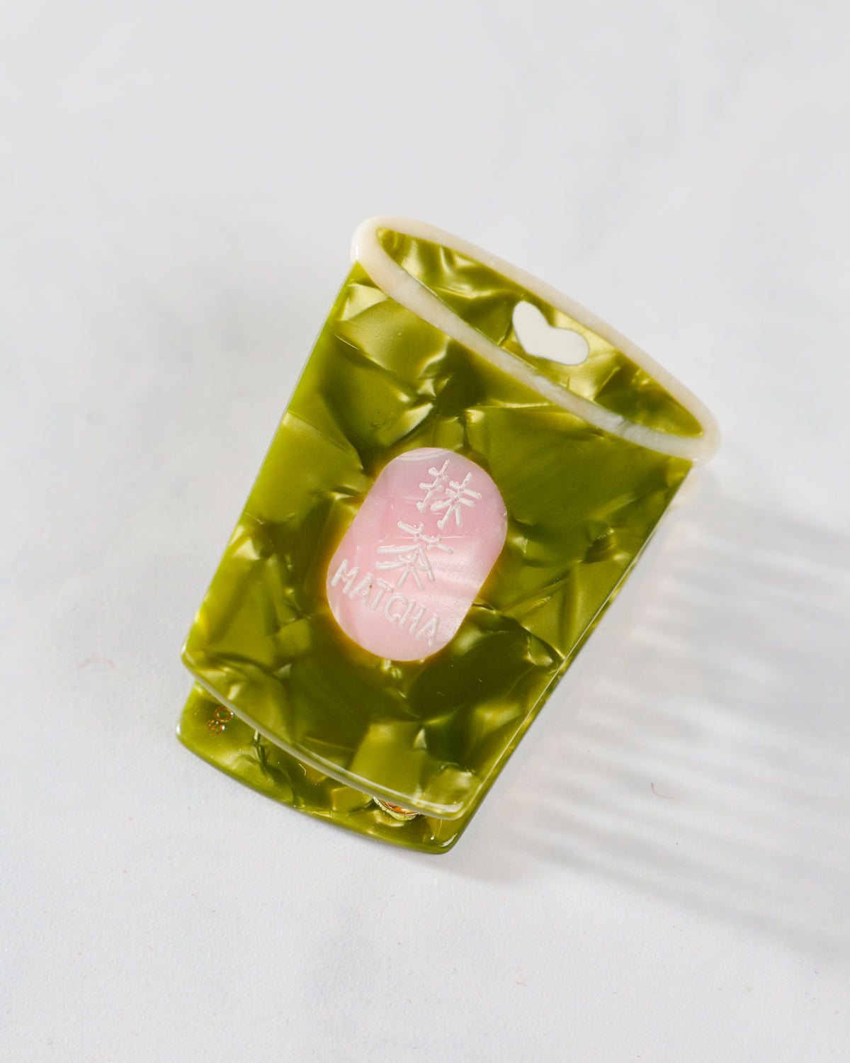 Green mini claw hair clip shown closed in its packaging, with a pink oval label and a hanging slot.