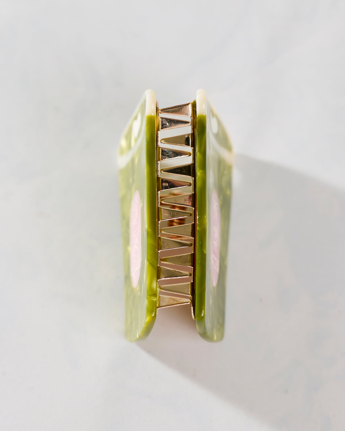 Side view of a green mini claw hair clip showing its metal hinge and interlocking teeth.